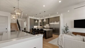 Una cocina moderna con una isla central, taburetes de bar, iluminación colgante y un refrigerador empotrado.