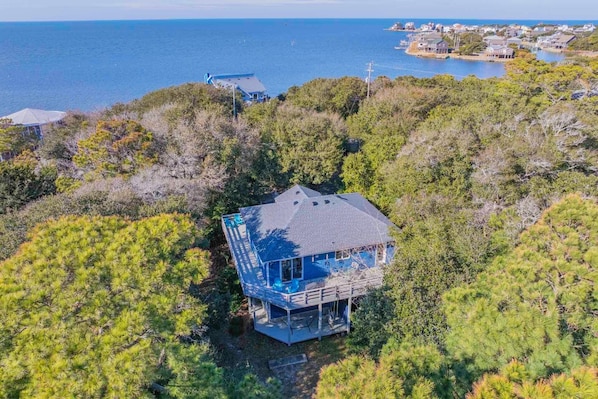 A coastal house with a large deck, surrounded by dense pine trees, overlooking the sea. - Brand New Peaceful Soundside Frisco Retreat, Dog Friendly (Frisco)