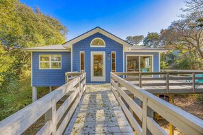 A blue building with a central door, two side wings, and a wooden deck leading to the entrance. - Brand New Peaceful Soundside Frisco Retreat, Dog Friendly (Frisco)