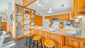 A kitchen with wooden cabinets, a central island with stools, and a microwave.