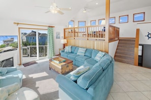 A spacious living room with a blue sofa, a wooden coffee table, and a view of a house through a sliding glass door. - Semi-Oceanfront, Dog Friendly Home in Waves with Pool, Hot Tub, Game Room (Waves)