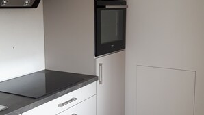 Una cucina compatta con mobili bianchi, un piano di lavoro nero, un forno integrato e un microonde.