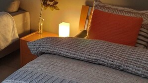 Un letto rifatto con una coperta a fantasia, una lampada da comodino e un vaso con un singolo fiore rosso.