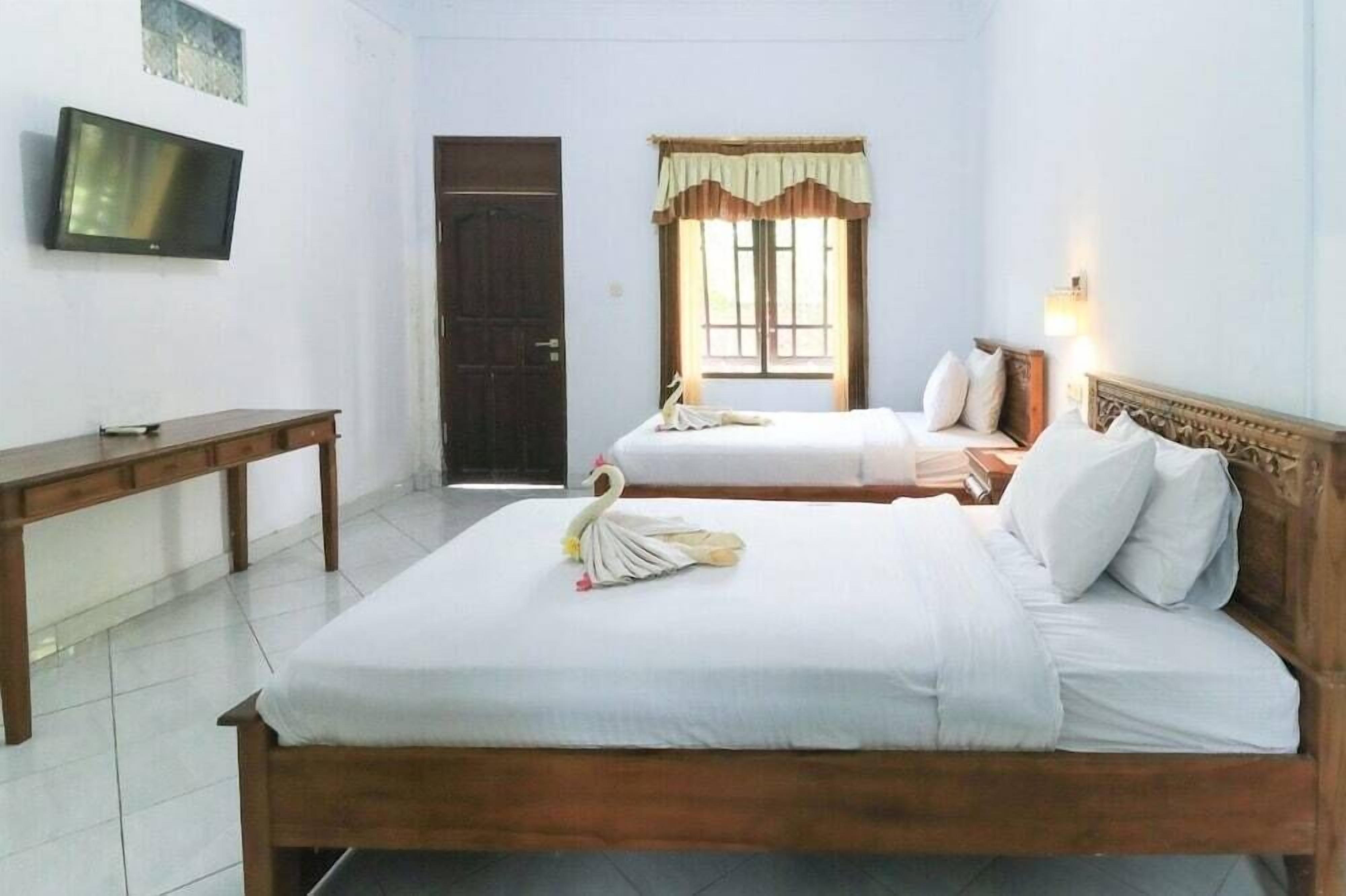 A hotel room with two beds, a TV, a desk, and a window with curtains.