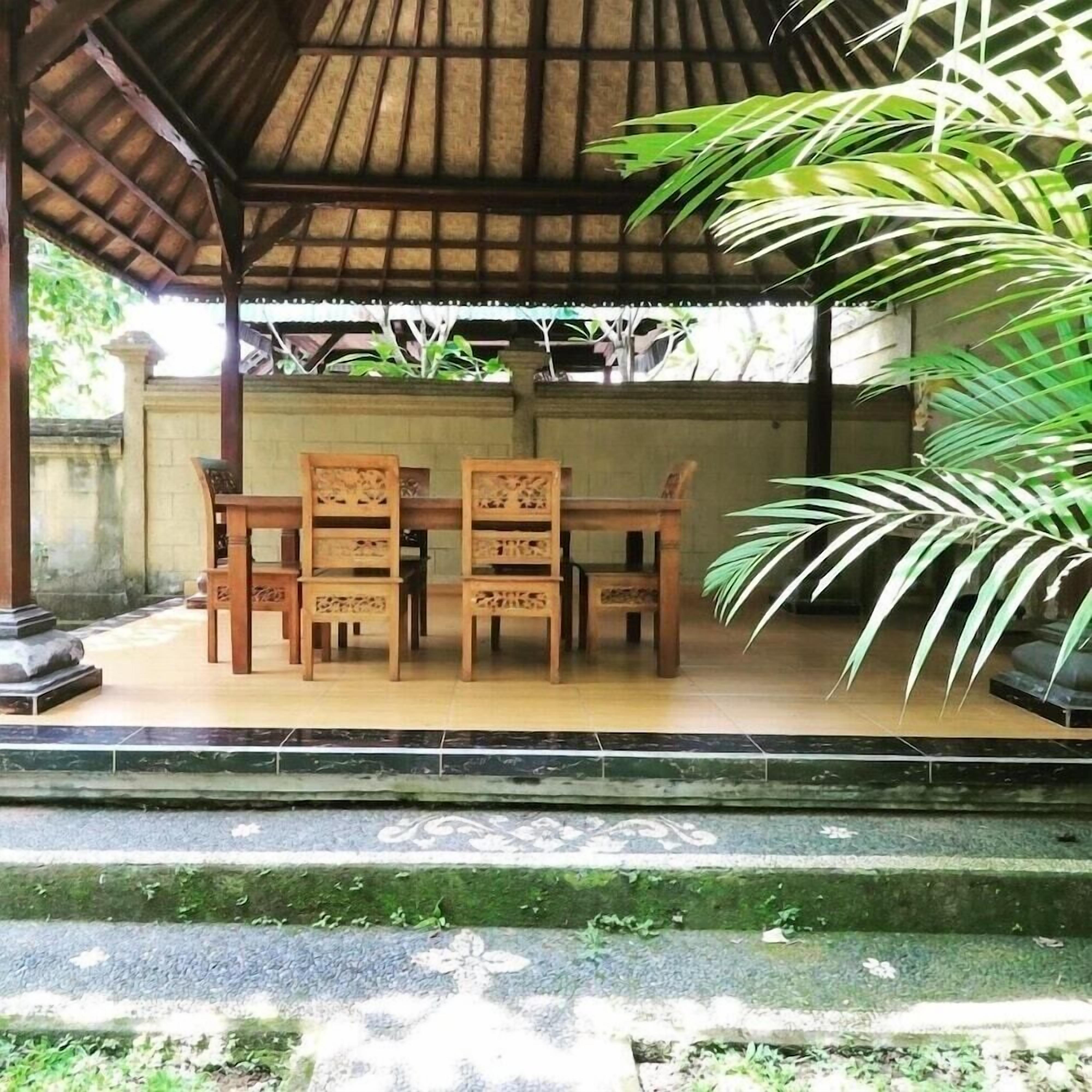 Un espace extérieur abrité, doté d’un sol carrelé, de chaises en bois et d’une grande plante en pot.