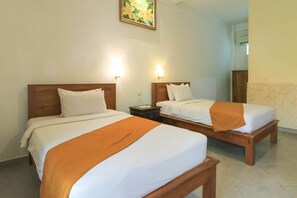 Duas camas lado a lado com cabeceiras de madeira, roupa de cama branca e um cobertor laranja.