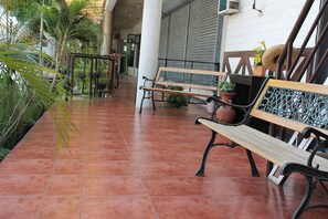 Uma área externa coberta com piso de azulejos, bancos, plantas em vasos e uma escadaria.
