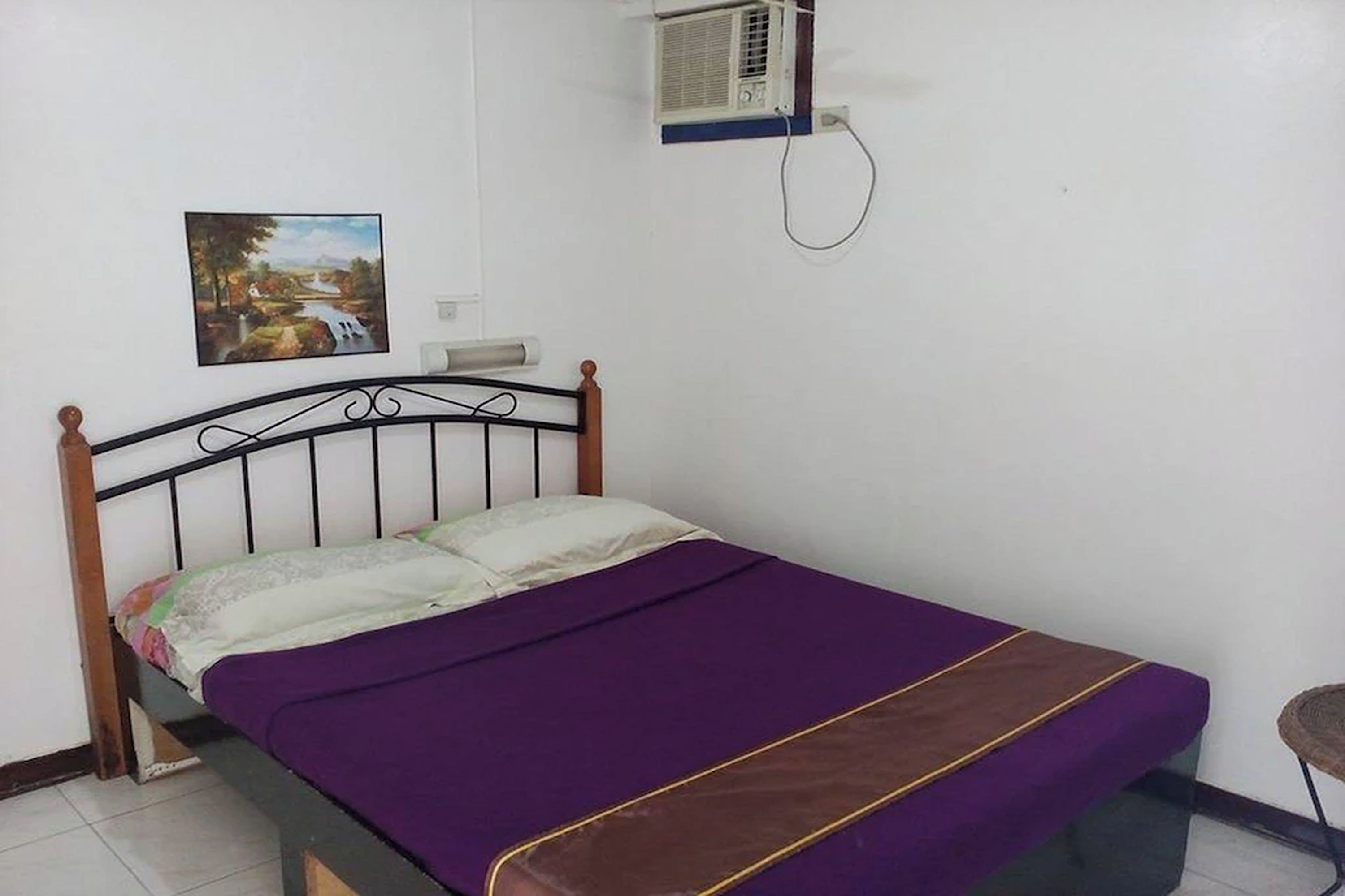 A single bed with a purple bedspread and a brown headboard in a room with white walls.