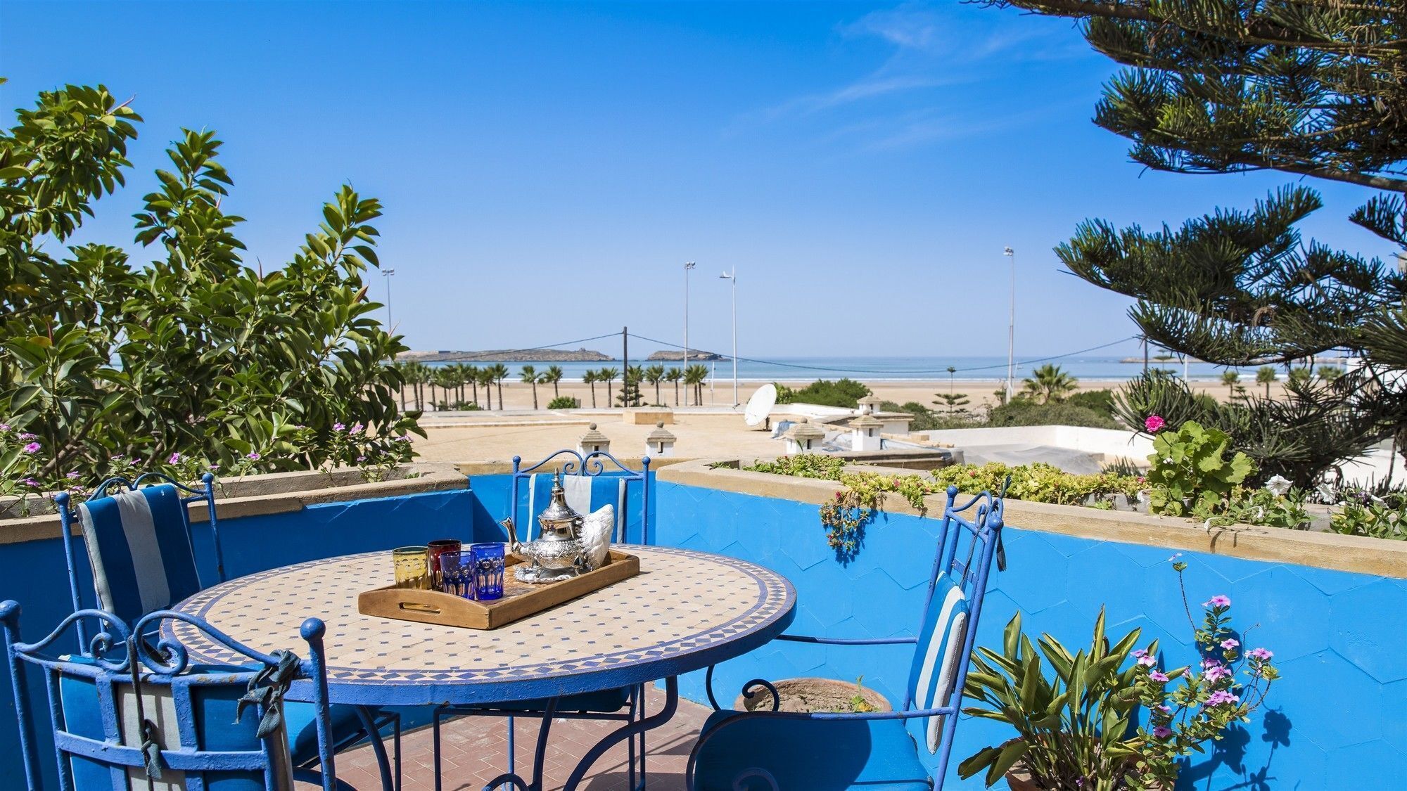A round table with a tray, chairs, and a view of the beach and ocean.