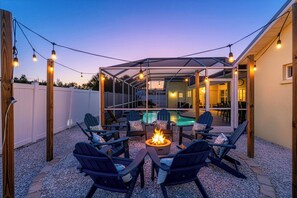 Une terrasse extérieure avec des fauteuils Adirondack, un foyer et un espace piscine aménagé sous une structure couverte.