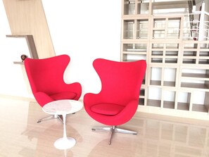 Twee rode stoelen met een kleine ronde tafel in een moderne kamer met een houten vloer en een witte muur.