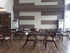 A spacious indoor area with multiple tables and chairs, a kitchen area in the background, and a modern wall design. - Hotel 88 Fatmawati (Jakarta)