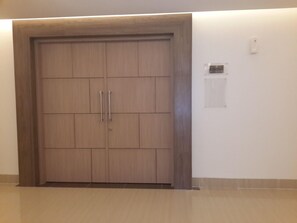 A closed wooden door with two handles, a white wall, and a small white electrical outlet. - Hotel 88 Fatmawati (Jakarta)