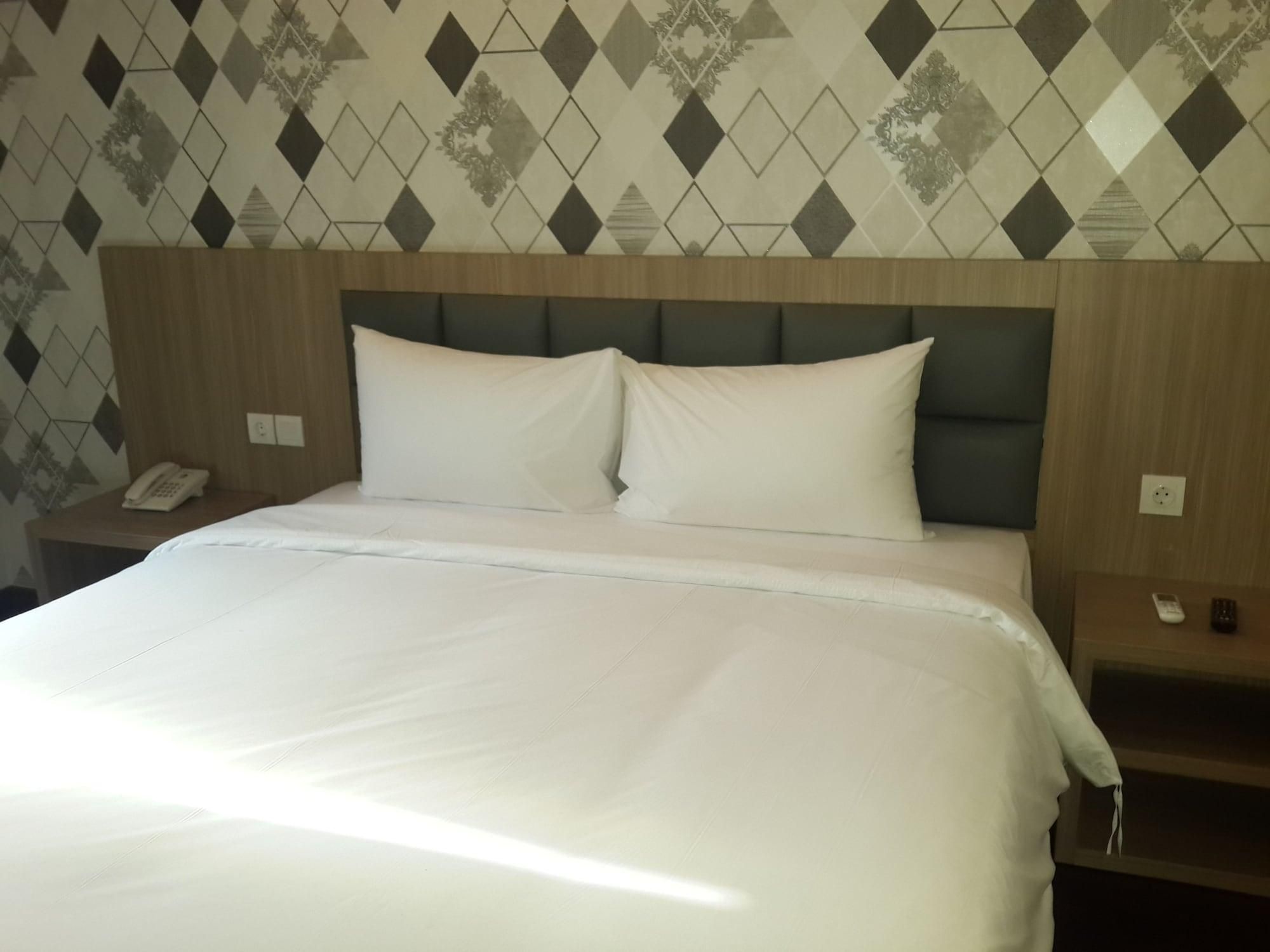 Een hotelkamer met een groot bed, een houten hoofdeinde, een telefoon en een nachtkastje.