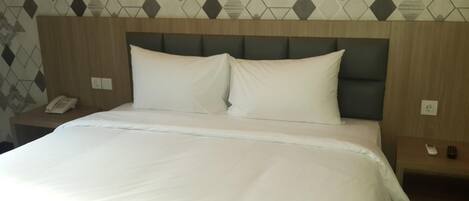 A hotel room with a large bed, a wooden headboard, a telephone, and a nightstand.