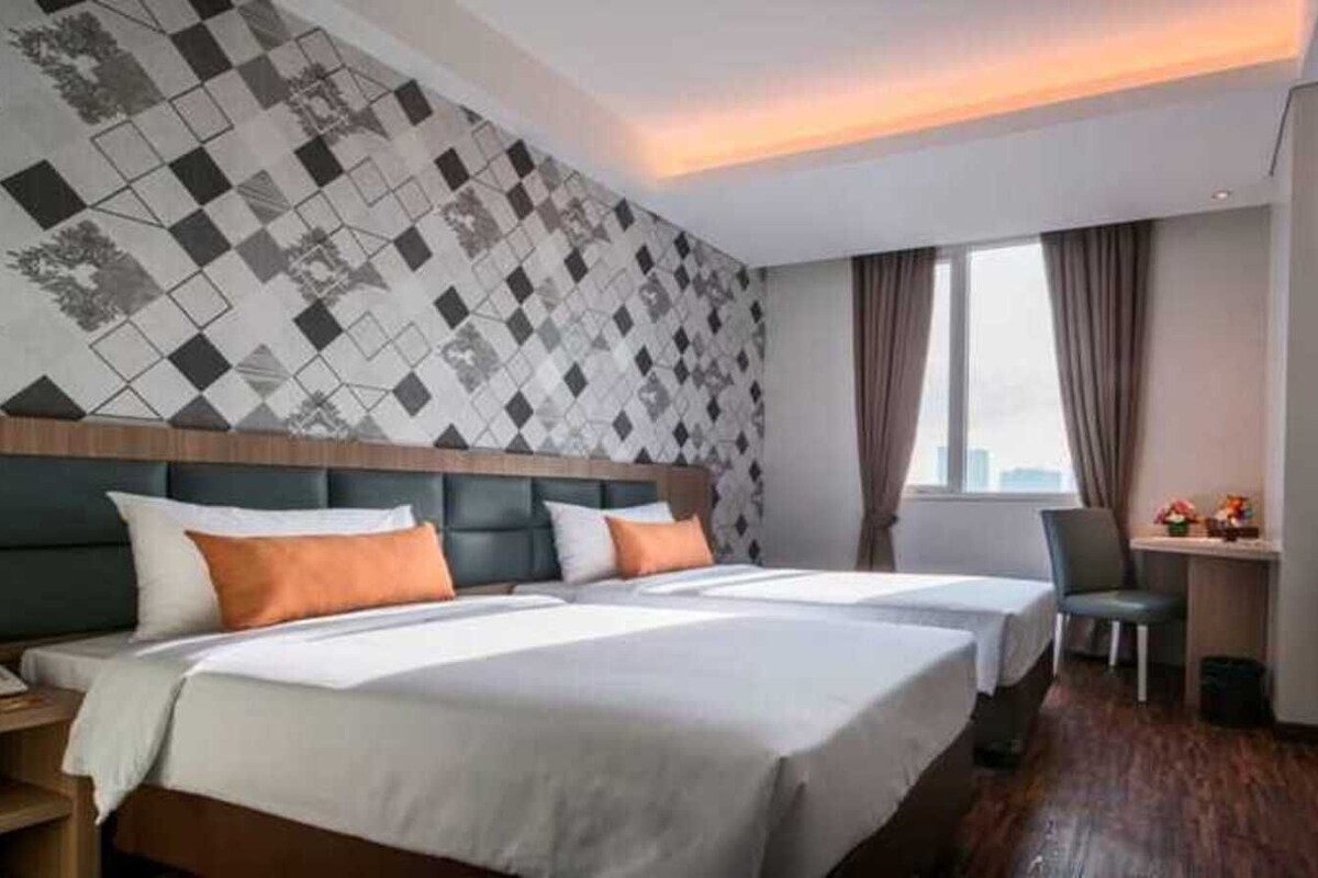 Habitación de hotel con dos camas, un escritorio, una silla, un televisor y un papel tapiz estampado.