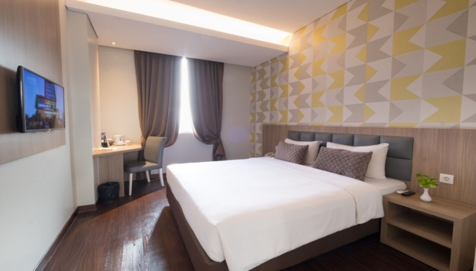 A hotel room with a bed, desk, chair, and a TV mounted on the wall.