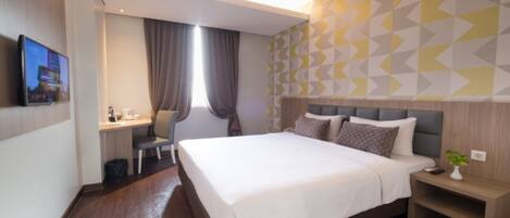 A hotel room with a bed, desk, chair, and a TV mounted on the wall.