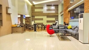 A modern interior with a dining area, a sofa set, a red chair, and a kitchen area. - Hotel 88 Fatmawati (Jakarta)
