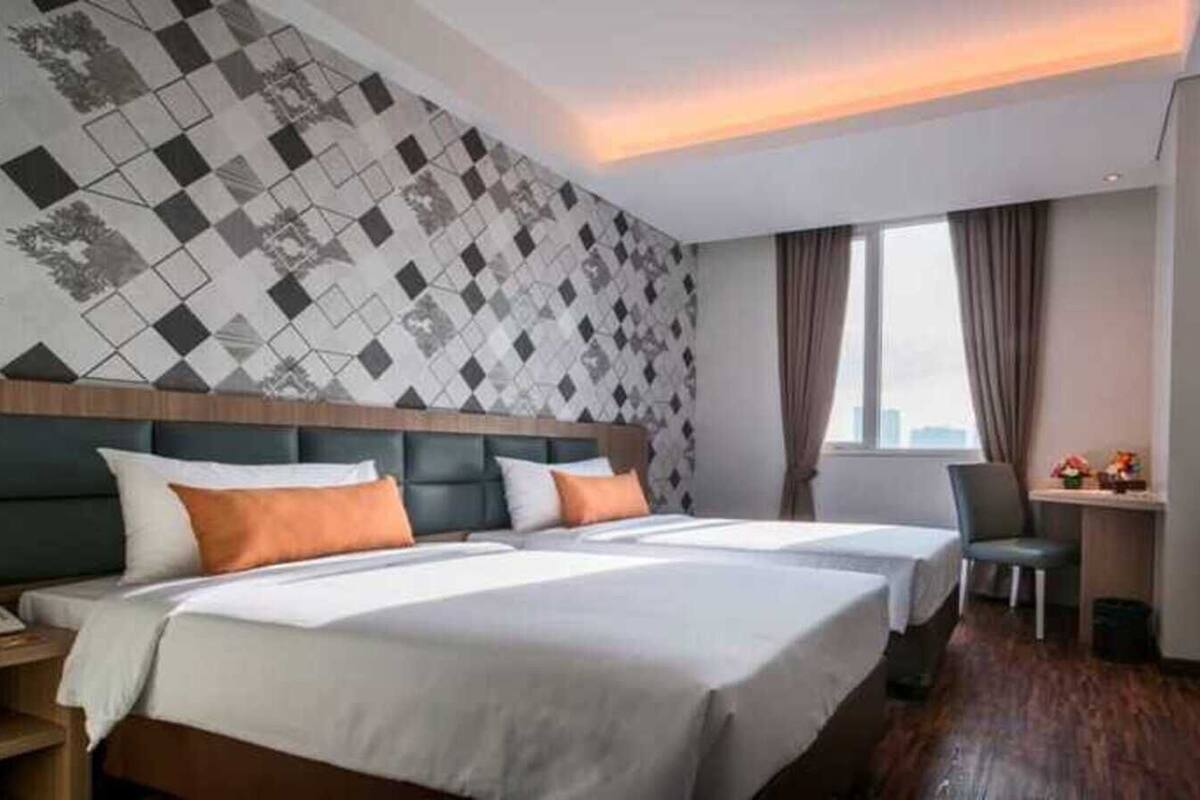 A hotel room with two beds, a desk, a chair, a TV, and a patterned wall.
