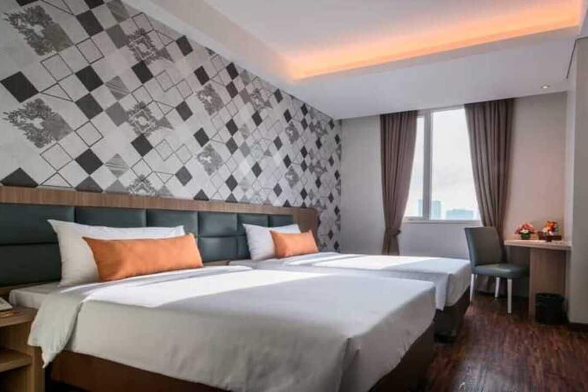 Ein Hotelzimmer mit zwei Betten, einem Schreibtisch, einem Sessel, einem Fernseher und einer Wand mit Muster.