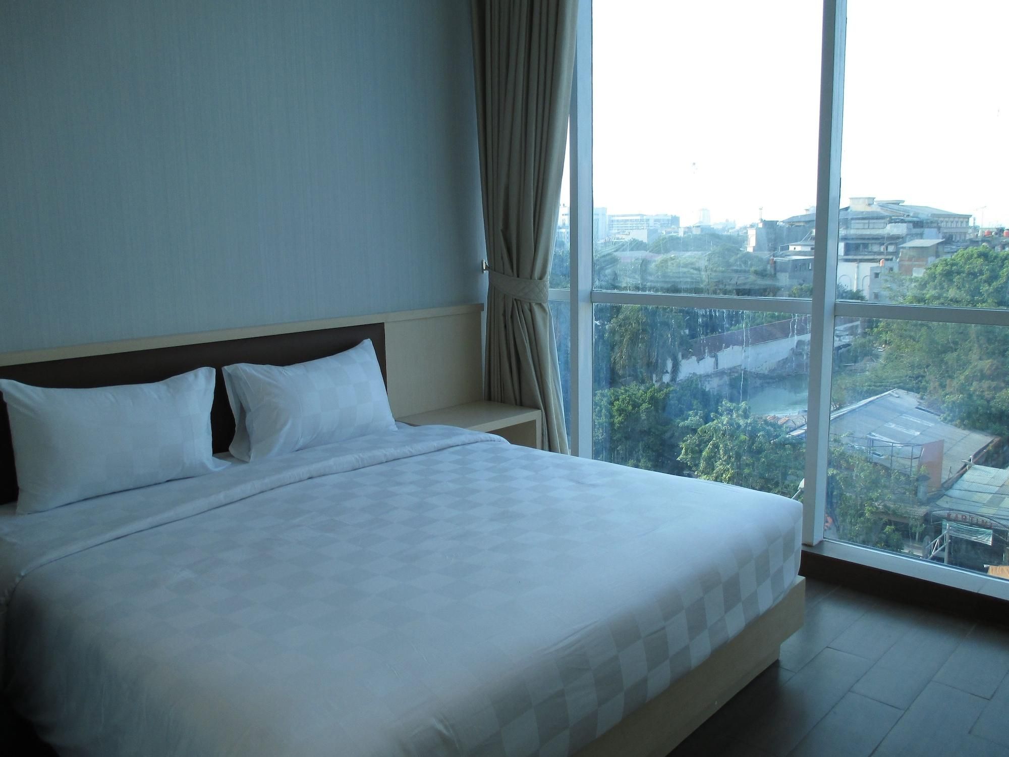 A hotel room with a large bed, a view of the city through a large window, and a curtain on the window.