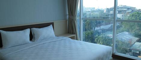 A hotel room with a large bed, a view of the city through a large window, and a curtain on the window.