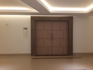 Una puerta de madera grande con dos manijas, un interruptor de luz y una pequeña señal en la pared a la izquierda.