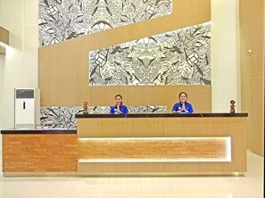 Een receptiebalie met een behangetapijt en twee medewerkers.