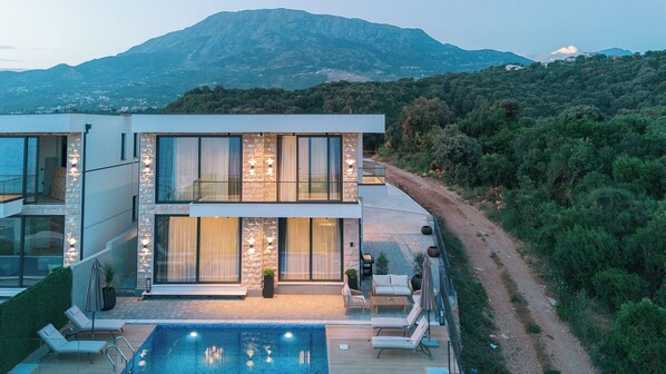 A modern two-story house with a swimming pool, large windows, and a view of a mountain.