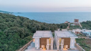 A modern two-story building with a flat roof, located on a hillside overlooking a body of water.