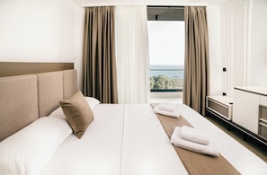 Ein Hotelzimmer mit einem großen Bett, einem Nachttisch und Blick aufs Meer.