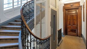 Una scala con ringhiere nere ornate e una balaustra in legno, che conduce a una porta in legno con un pannello decorativo.