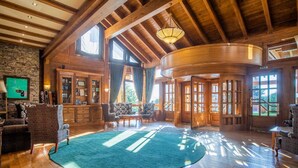 A spacious room with wooden beams, large windows, a fireplace, and a green carpet. - Pirin Golf Country Club Apartments (Razlog)