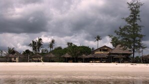 A beach resort with thatched-roof huts, palm trees, and a large building with a balcony. - Kipepeo Beach and Village (Dar es Salaam)
