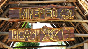 Twee houten borden met gele omlijningen, waarvan één 'KIPEPEO' en de ander 'STRAND' zegt.