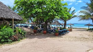 A beachside resort with thatched-roof structures, picnic tables, and lounge chairs.