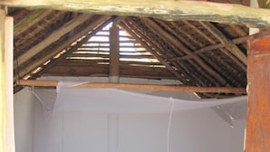 A single bed with a wooden frame and a mosquito net in a room with a sloped ceiling and a striped floor. - Kipepeo Beach and Village (Dar es Salaam)