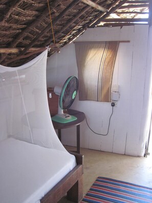 Een kamer met een bed, een ventilator en een raam met gordijnen.
