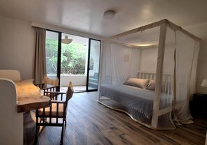 A bedroom with a canopy bed, a desk with chairs, and a view of greenery outside.