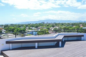 A rooftop terrace with a wooden deck, white walls, and a black railing.