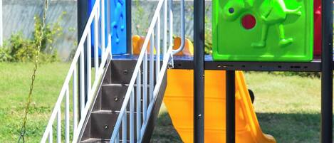 A playground with a metal staircase, a yellow slide, and a blue climbing structure.