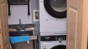 A compact laundry area with a stacked washer and dryer, a sink, and a drying rack. - Resort Like Amenities - Accommodation In The City (Kingston)
