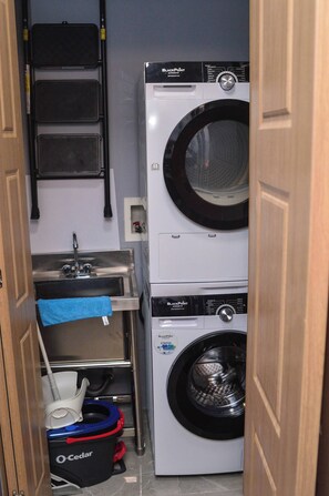 Een kleine wasruimte met een gestapelde wasmachine en droger, een wasbak en een droogrek.