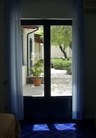Una habitación con puerta de vidrio corredera que da a un balcón con plantas en macetas y un árbol.