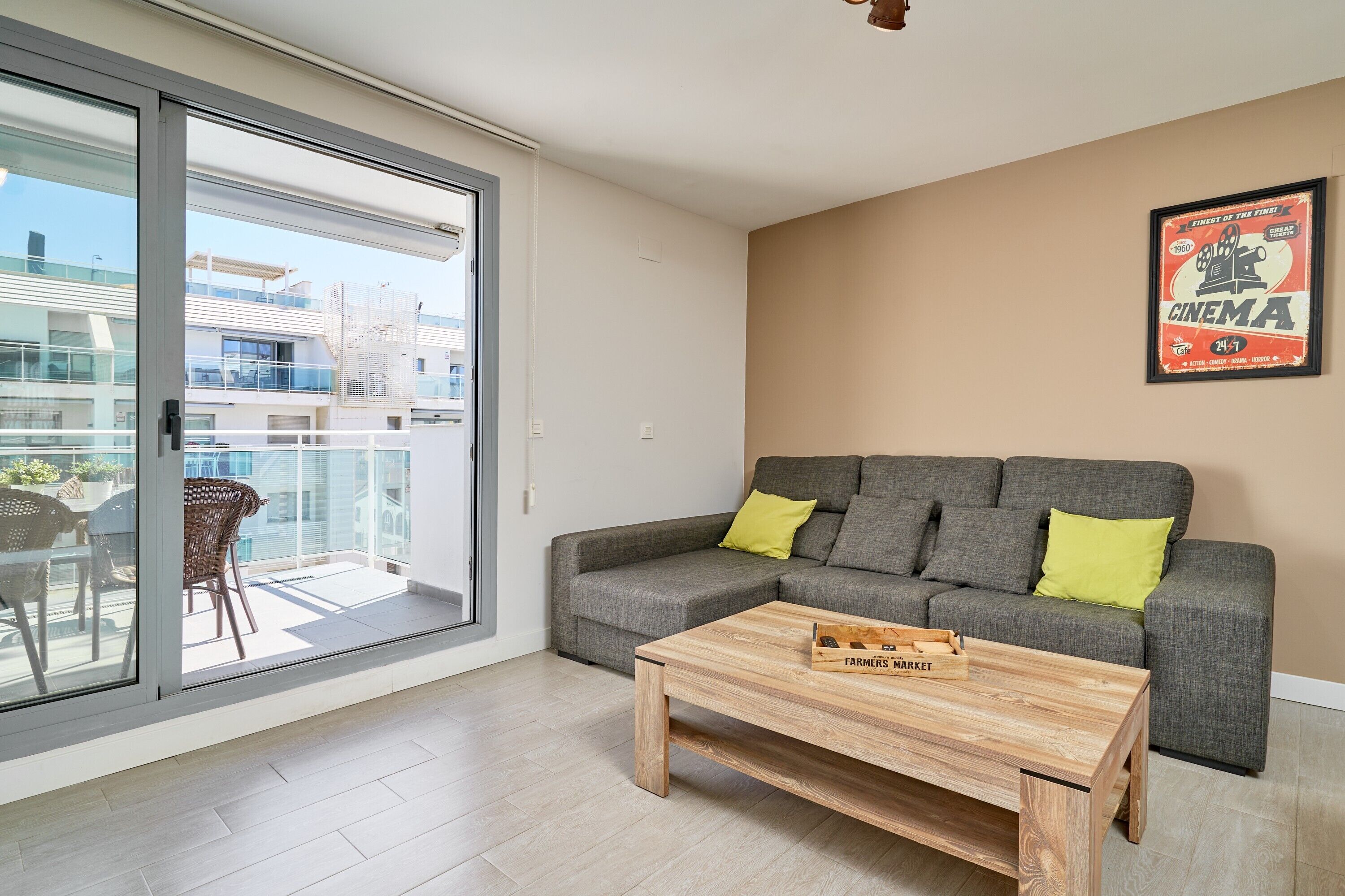 A living room with a grey sofa, wooden coffee table, and a balcony with outdoor furniture.
