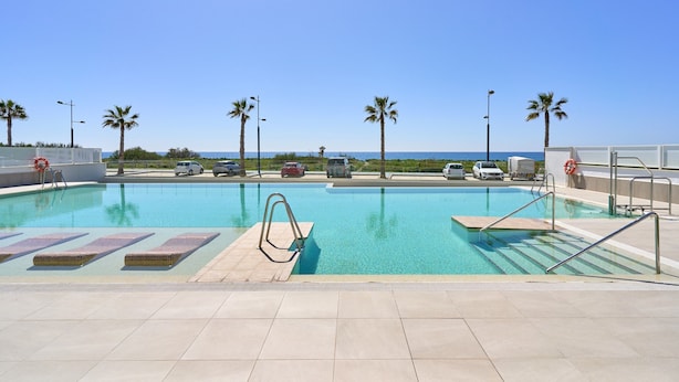 A swimming pool with clear blue water, surrounded by palm trees and a view of the ocean. - 'Apartamento caracoles Duna Beach' with Sea View, Wi-Fi, and Air Conditioning (Torrox)