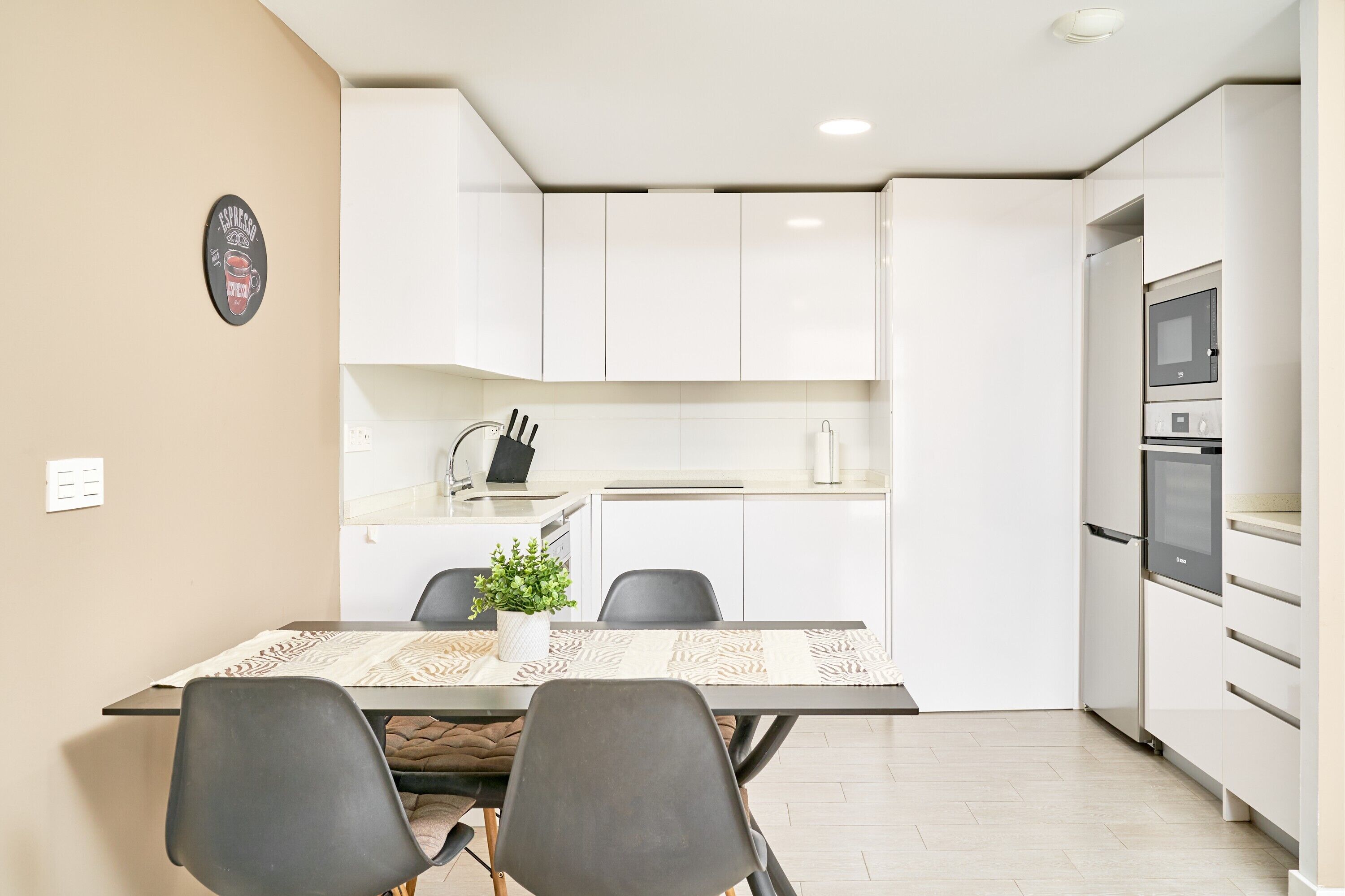 A compact kitchen with white cabinets, a microwave, and a refrigerator. There is a dining table with a placemat and two chairs.