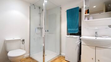 Un baño con ducha de vidrio, inodoro, lavamanos y espejo sobre el lavamanos.