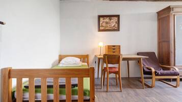 A room with a wooden bed, a desk with a lamp, a chair, and a wardrobe.